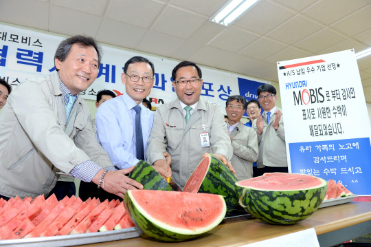 27일 현대모비스 협력사 중 한 곳인 ㈜유라하네스에 방문한 노태호 현대모비스 통합구매담당 상무(앞 줄 가운데)라 유상근 ㈜유라하네스 사장(앞줄 오른쪽)과 함께 직원들에게 나눠 줄 수박을 자르고 있다. <현대모비스 제공>